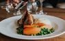 Sauce being poured onto a plate of food with chicken breast and vegetables.