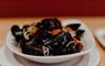 A white bowl filled with Hebridean mussels, garnished with diced tomatoes, parsley, and linguine.