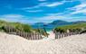 A picturesque view of Vatersay, Isle of Barra, with a wooden fence and gate opening to sandy dunes and the beach beyond.