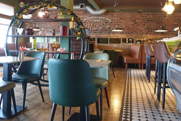 HS1 cafe bar interior with table and charis in a tan and teal colourway and exposed brick wall at rear.