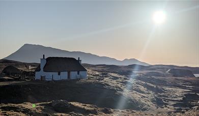 Sun shine on Glaic Cottage with hill behind.