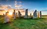 Callanish Stones, Isle of Lewis. Large standing stones set on green grass and sun setting in the background.