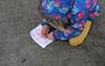 Photo of a small child drawing on a piece of paper on a sandy beach.