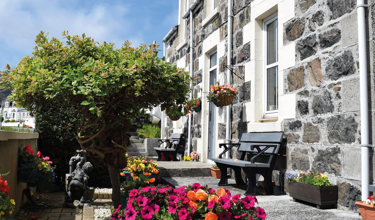 Tigh na Mara, Isle of Barra - stone exterior of the guesthouse with bench and flowers Tigh na Mara, Isle of Barra - stone exterior of the guesthouse with bench and flowers