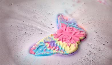 A pink, blue and yellow butterfly bath bomb dissolving in water.