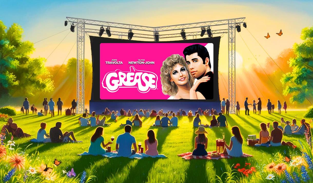 The film 'Grease' on a big screen outside with people on picnic blankets watching it.