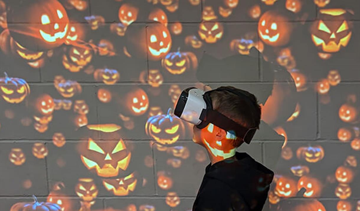 little boy with vr headset on and pumpkin background.