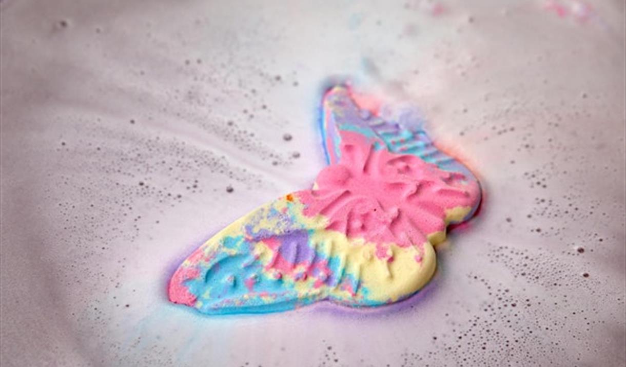 A pink, blue and yellow butterfly bath bomb dissolving in water.