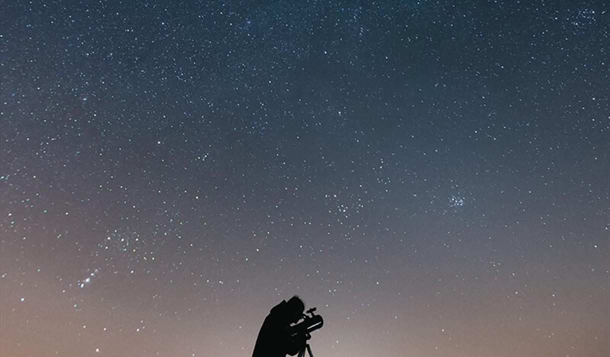 Man looking through a telescope under the night sky