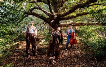 Three people walking through and dancing in a forest.