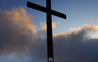 A giant cross stands against a blue, cloud-filled sky.