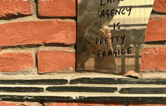 A brick wall featuring a piece of mirror reflecting a woman holding a phone