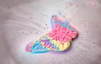 A pink, blue and yellow butterfly bath bomb dissolving in water.
