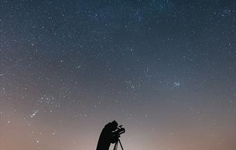 Man looking through a telescope under the night sky