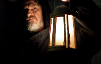 A man holding a lantern in the dark. Text reads: The Priestgate Vaults.