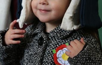 A picture of a young child in a coat wearing a Tudor hat and a Tudor rose badge