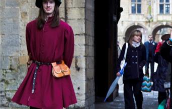 A man dressed in Tudor clothing, walking with a tour group around the grounds of Peterborough Cathedral