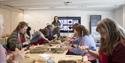 Participants sitting around a table making jewellery with the workshop leader stood at the front