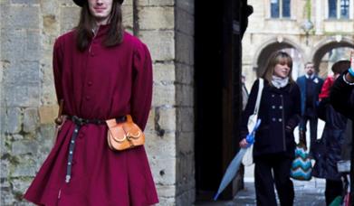 A man dressed in Tudor clothing, walking with a tour group around the grounds of Peterborough Cathedral