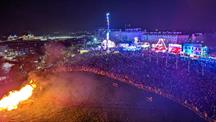 A bonfire on the left of the image with crowds of people on the right watching on 