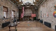 Spacious stone-walled art gallery with colourful works on display.