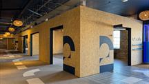 Interior of a modern building with wooden panel walls, black accents, and large painted numbers. The space features open doorways, patterned flooring, and hanging woven light fixtures