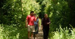 A National Trust Ranger giving a tour to visitors in a green woodland setting.