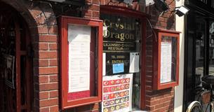 The red brick exterior of the restaurant with menus in red glass cases, pictures of various dishes and signage.