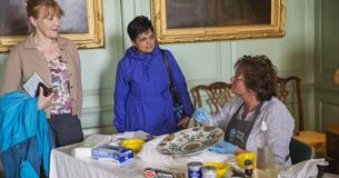 A conservator showing visitors how she cleans and cares for a ceramic dish