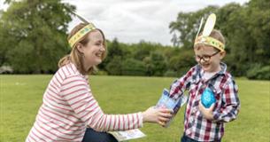 A woman and a young child in paper Easter bunny ears laughing and sharing a chocolate egg