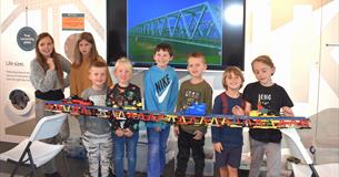 A line of children holding a long track made of lego.