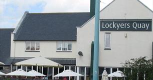 The outside of Lockyers Quay with outside seating and parasols in the foreground.