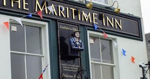 The pale green painted outside of The Maritime Inn with a painted figurehead affixed to the building and Union Jack bunting.