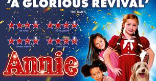 Children and dog stand amongst confetti. Annie is central in a red dress.