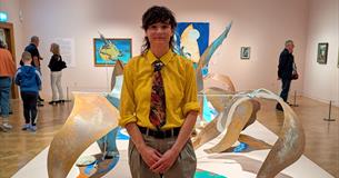 Photograph showing an artist in a gallery in front of their sculptural artwork