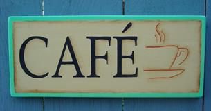 A sign bearing the word CAFE and a picture of a steaming cup of coffee. This hung on a blue painted fence.