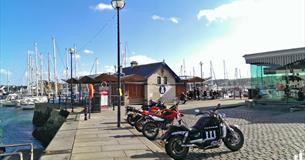 A distant shot of Cap'n Jaspers at the end of the quay with yachts in the background and motorbikes parked outside.