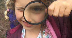 Child looks at camera through magnifying glass