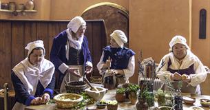 A group of people dressed in Tudor costume cooking in a historic kitchen