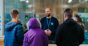 A man addresses a group of attentive individuals, standing at the forefront and sharing his insights.