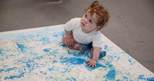 Photograph of a child sitting on a map which has blue paint on it