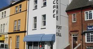 The outside of the Port O'Call Café showing brightly coloured awnings, outdoor tables and chairs and adjacent terraced properties.