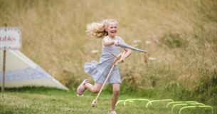 A girl on a hobby horse with a toy lance pretending to joust