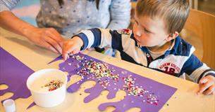 A toddler playing with arts and crafts at the aquarium as their parents looks over them