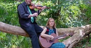 Two musicians sat on a fallen tree in the woods