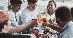Crowd around a pizza with drinks