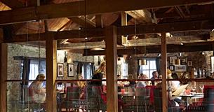 The inside of Miller & Carter with wooden beams, stone walls and diners sat at tables on black and red chairs.