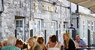 Customers sat at outside seating and tables in front of The Ship. Glass partitions separate the tables and there are large parasols overhead.