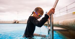 A child climbing up a ladder out of a swimming pool at Tinside Lido