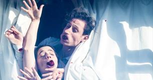 A man and a women are shown with their face and bodies squashed against the glass of a window.